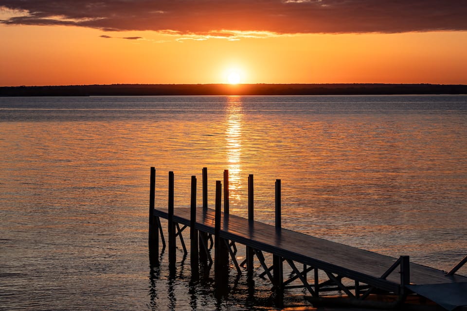 A sunset over a calm body of water with a wooden pier extending into the water.