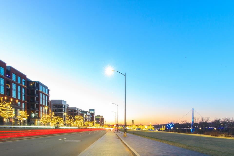 A city street at dusk with illuminated buildings and trees.