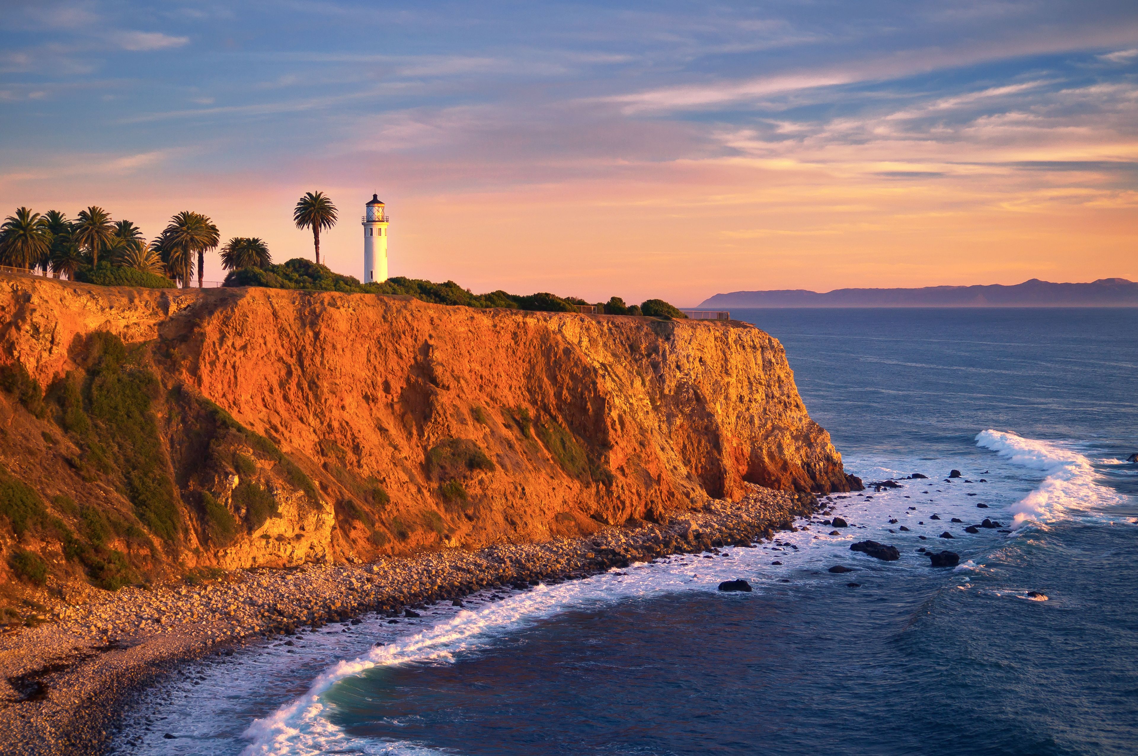 A coastal landscape with a lighthouse, palm trees, and a rocky cliff overlooking the ocean.