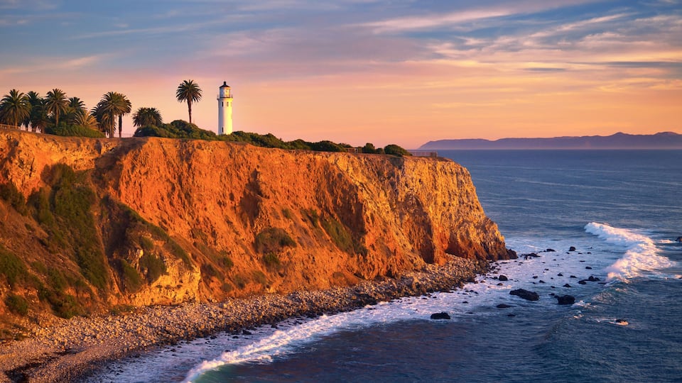 A coastal landscape with a lighthouse, palm trees, and a rocky cliff overlooking the ocean.