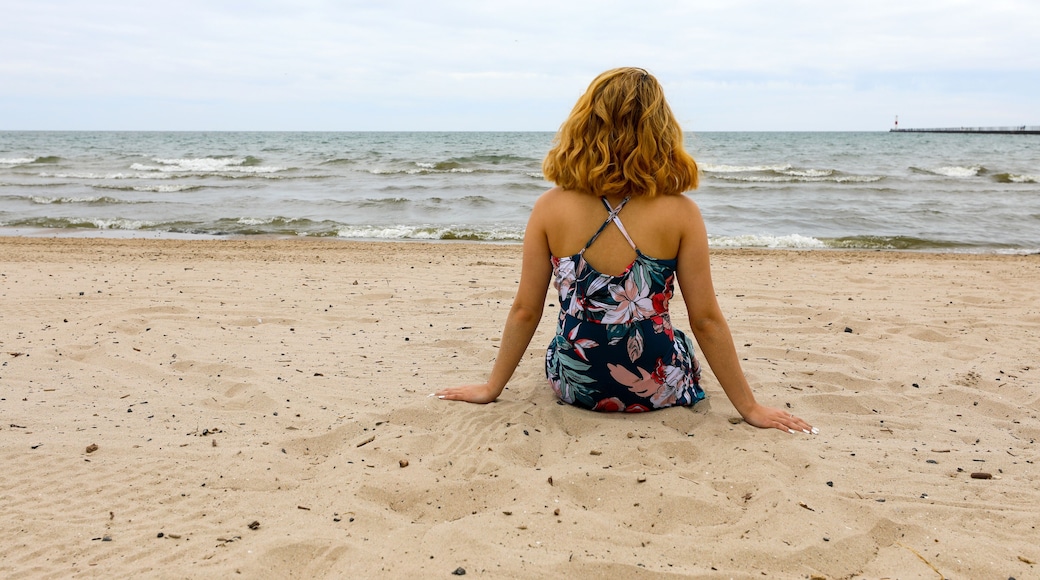 Iemand zit op een zandstrand, met de oceaan op de achtergrond.