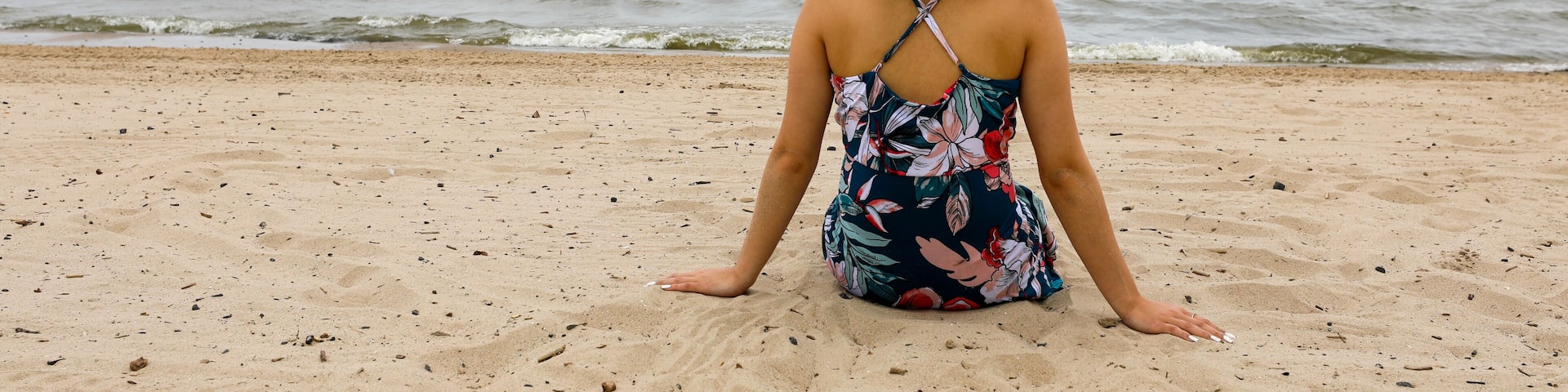 A person sitting on a sandy beach with the ocean in the background.