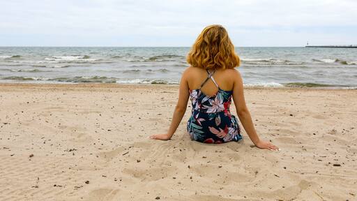 A person sitting on a sandy beach with the ocean in the background.