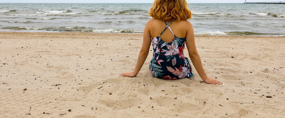 A person sitting on a sandy beach with the ocean in the background.