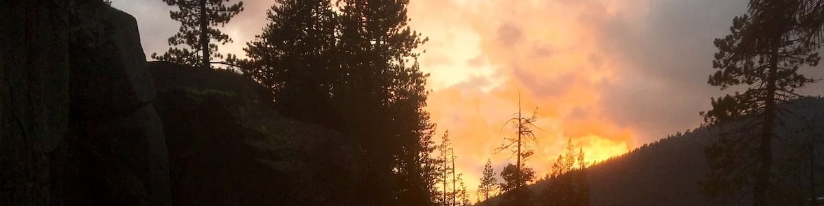 Une rivière qui traverse un paysage rocheux, avec des arbres et un coucher de soleil en arrière-plan.