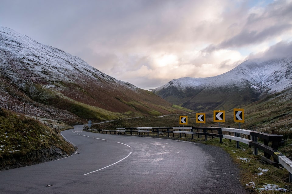A winding mountain road with snow-covered hills and directional signs.