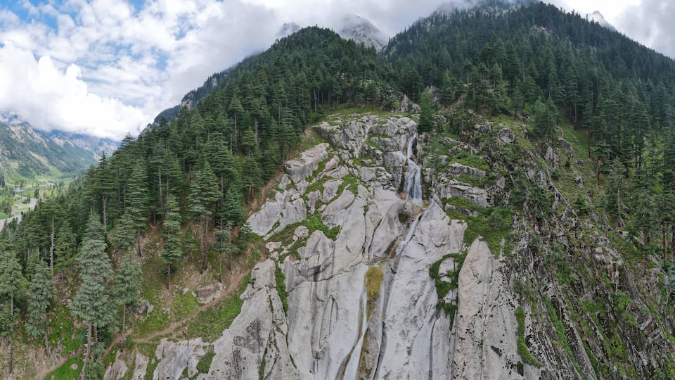 A mountainous landscape with a waterfall cascading down a rocky cliff, surrounded by dense forests.