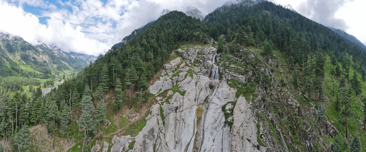 A mountainous landscape with a waterfall cascading down a rocky cliff, surrounded by dense forests.