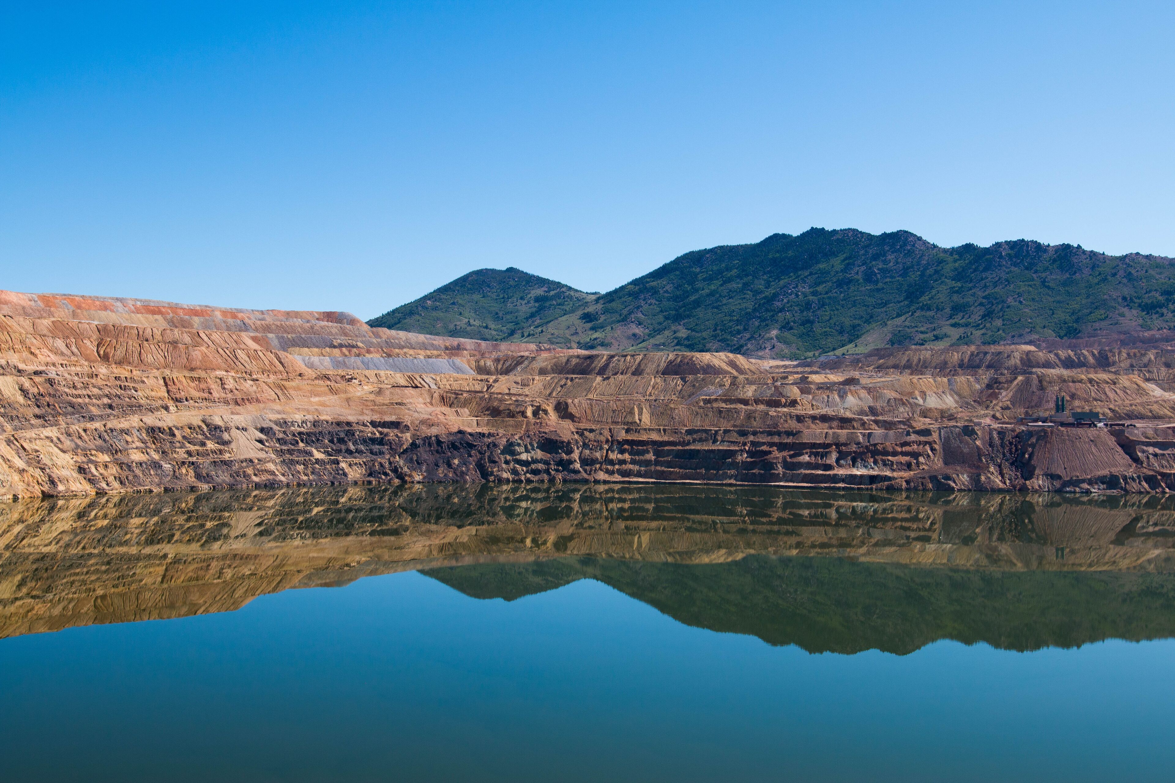 Uma grande mina a céu aberto com reflexo nítido na água, rodeada por montanhas.