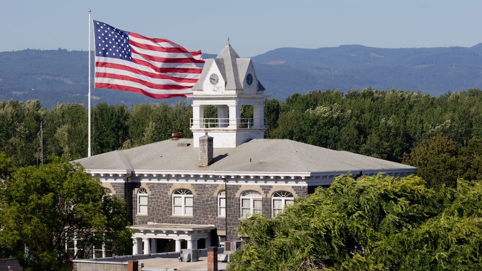 A historic building with a clock tower, surrounded by lush greenery and mountains in the background.