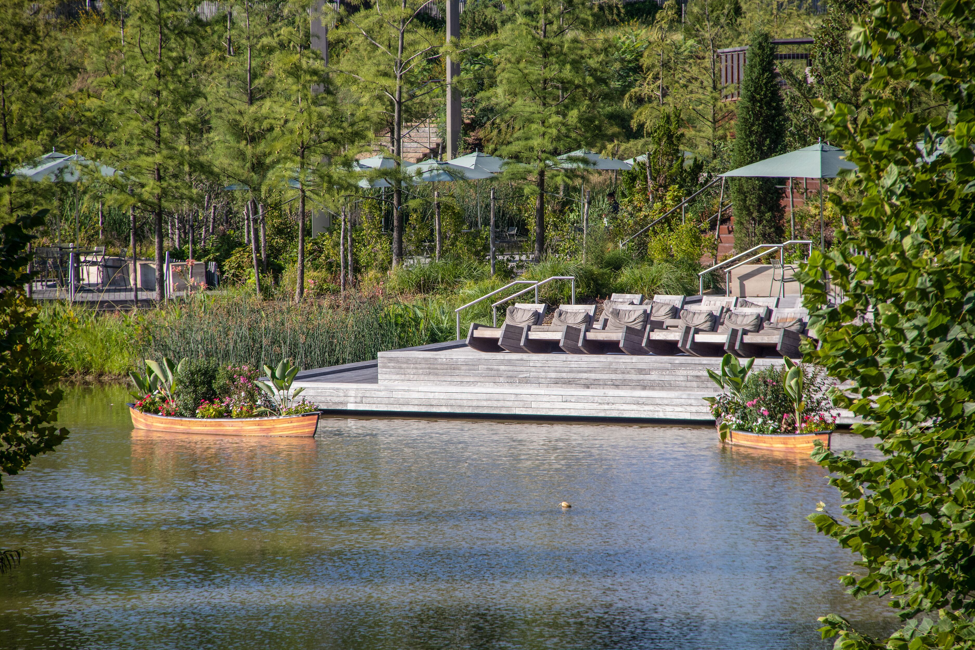 The Gathering Place - Award winning public park in Tulsa OK USA - Wooden deck with chairs beside pond with rowboats filled with flowers and tables and umbrellas and trees behind - selective focus