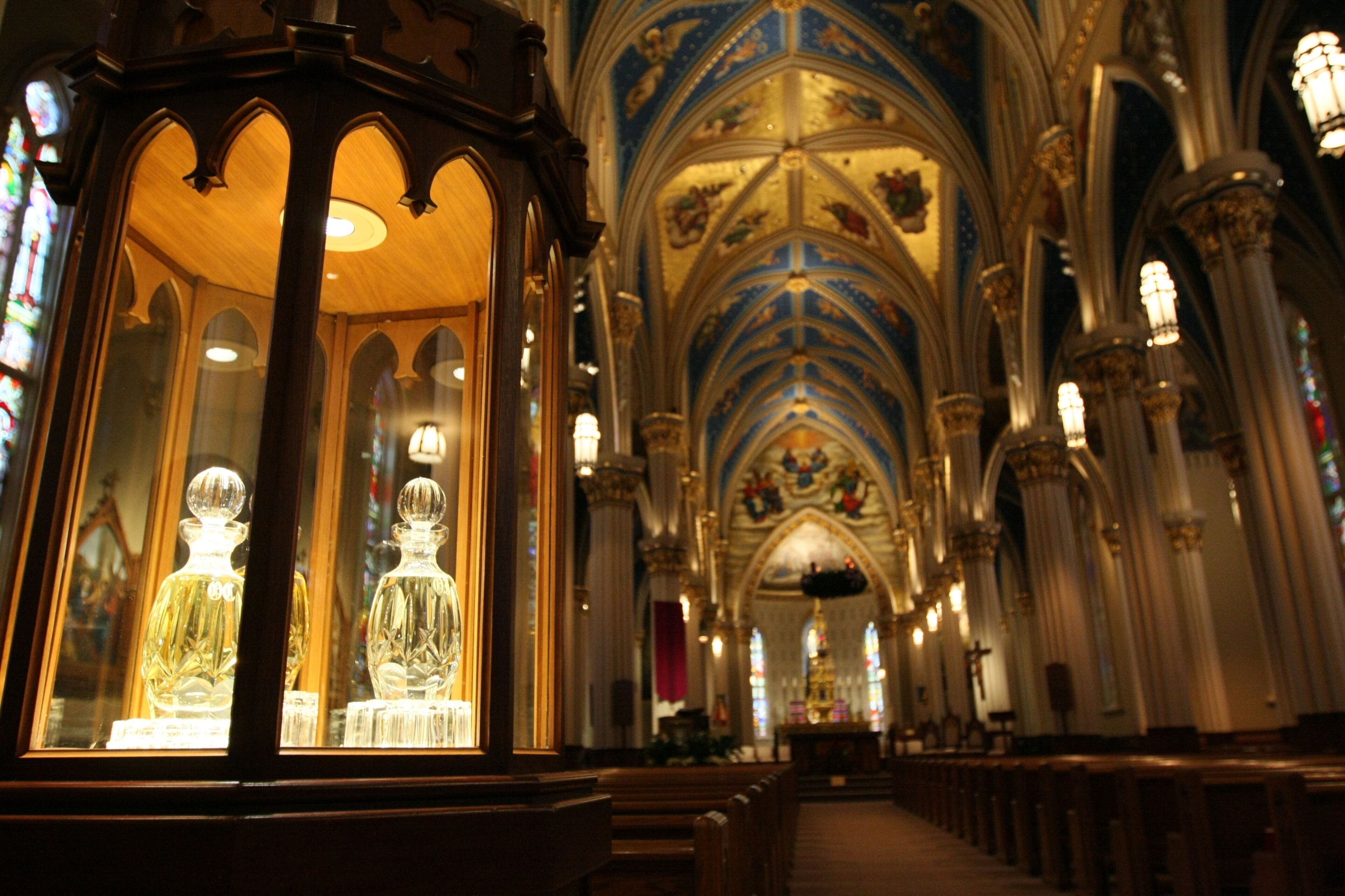 Interior de iglesia con vidrieras ornamentales, un techo abovedado alto y hileras de bancas.