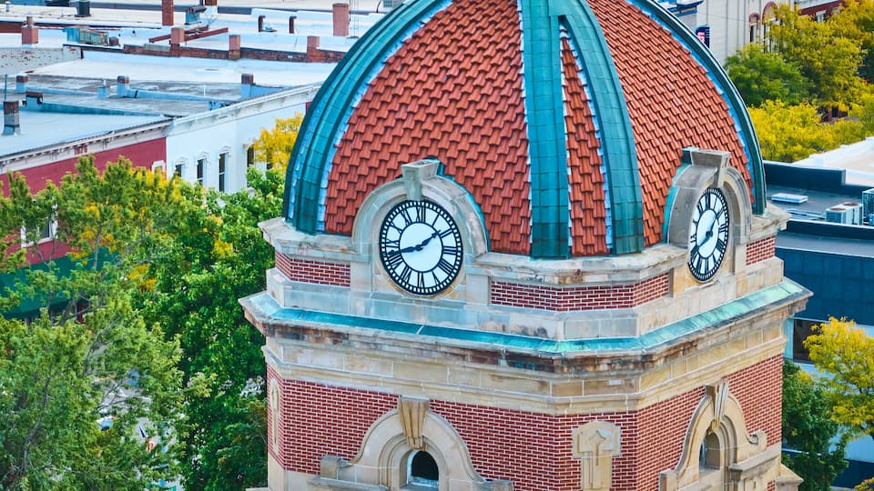 A clock tower with a red brick base and a dome with green and red tiles.