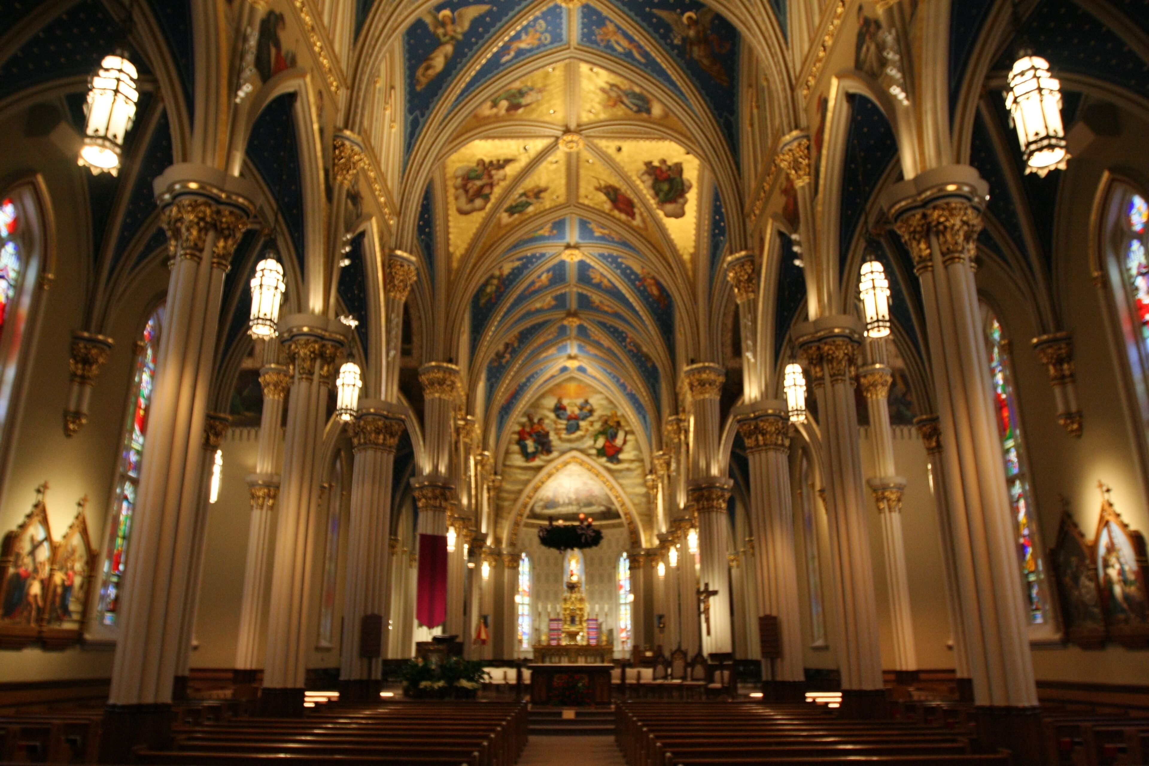 Interior de una catedral con techos abovedados altos, vidrieras y columnas ornamentales.