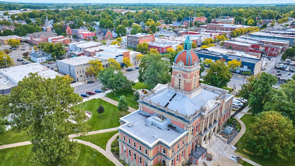 An aerial view of a town with a prominent clock tower, surrounded by historic buildings and green spaces.