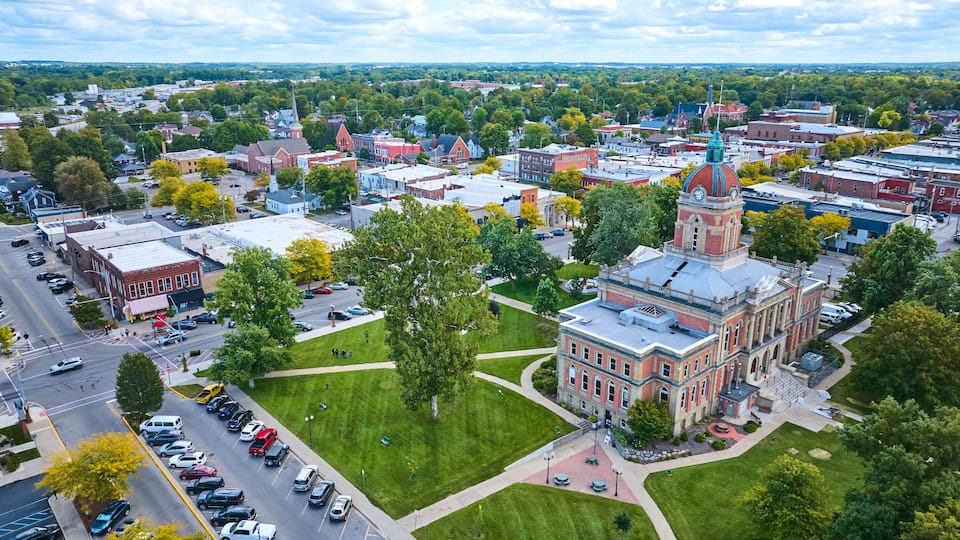A town with a prominent clock tower, a central green park, and a mix of historic and modern buildings.