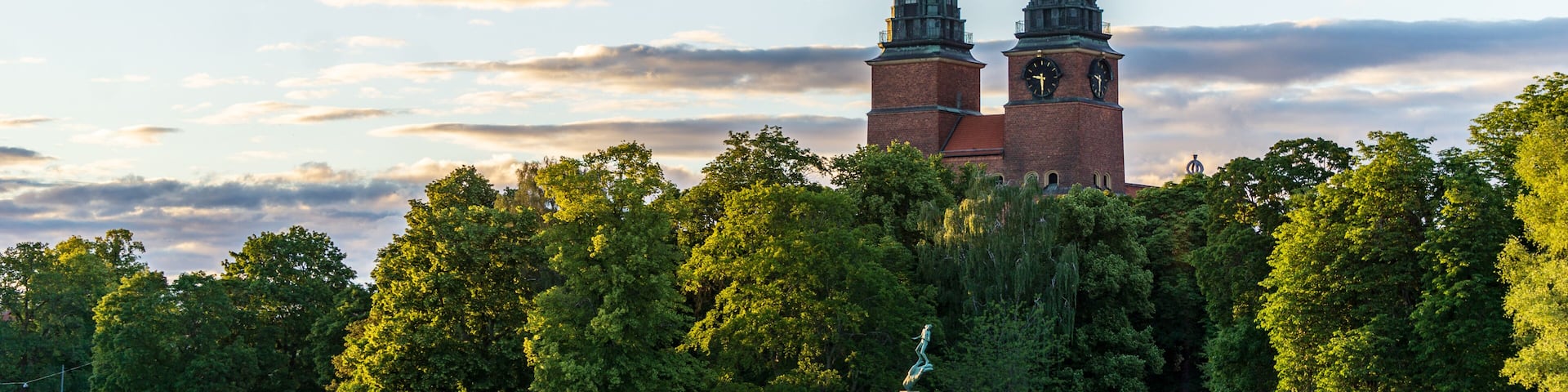 A historic church with twin towers, a calm lake, and lush trees.