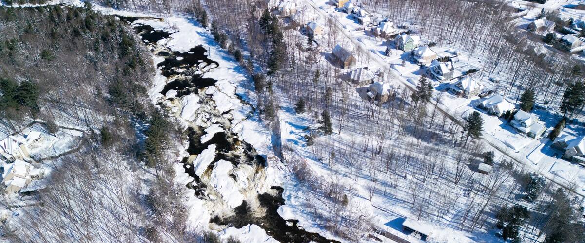 A snow-covered landscape with a river, houses, and a bridge.