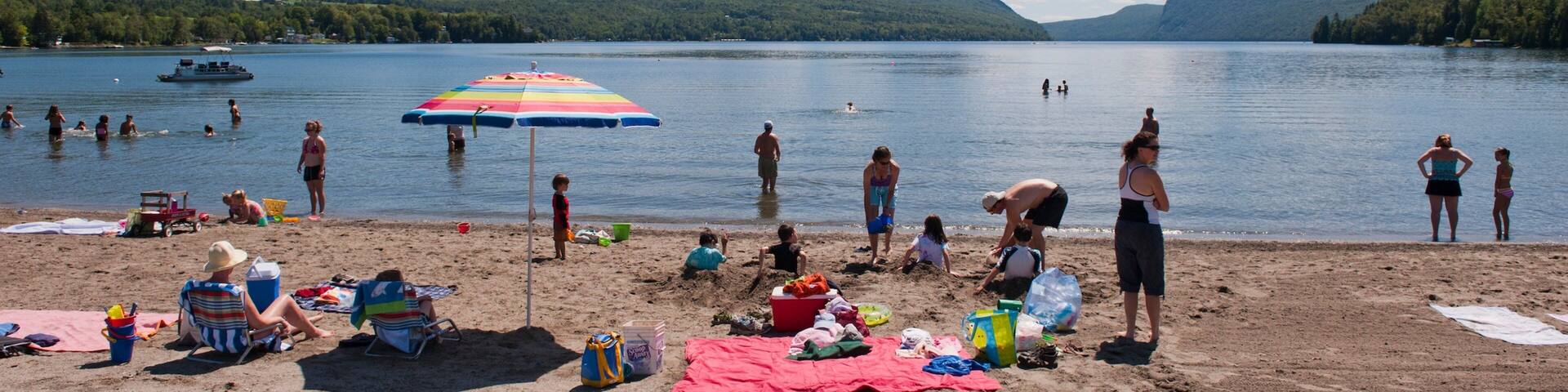 A lakeside beach with people swimming and sunbathing.