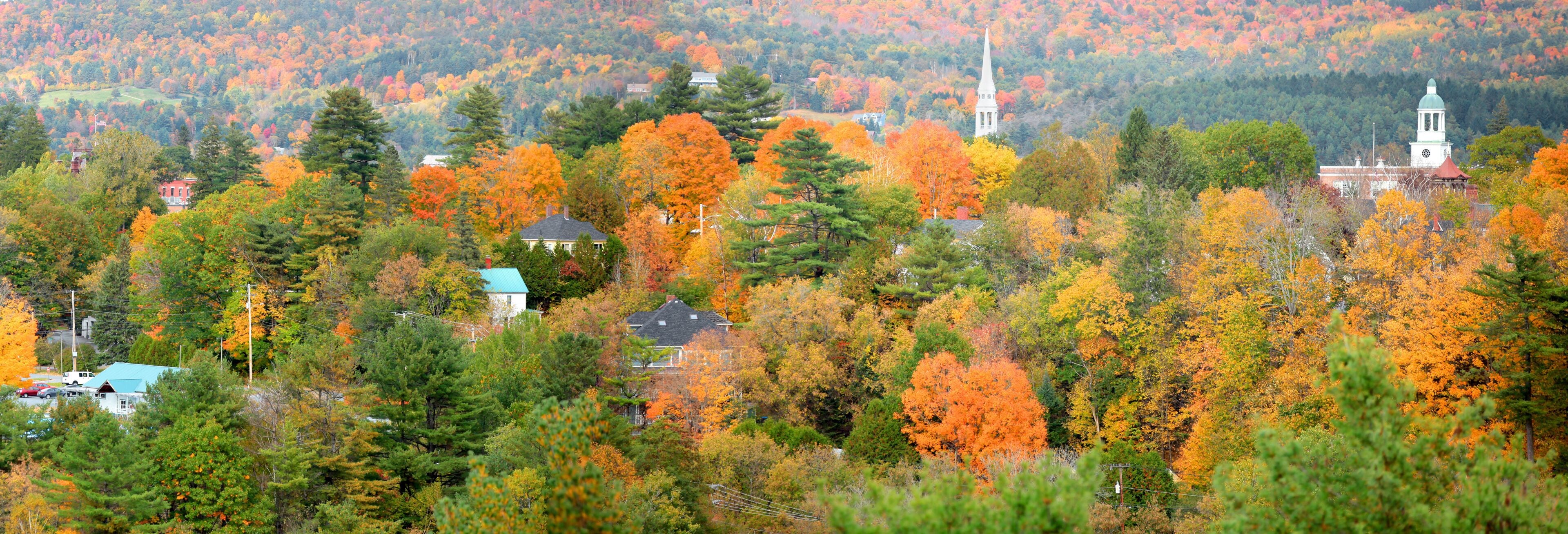 A town nestled among autumn-colored trees with a prominent church steeple.