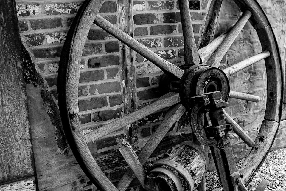 A large wooden wheel against a brick wall.