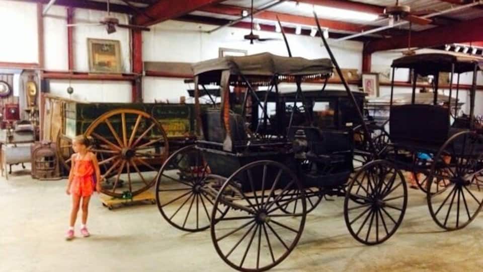 A vintage carriage in a museum with large wooden wheels and a covered seat.