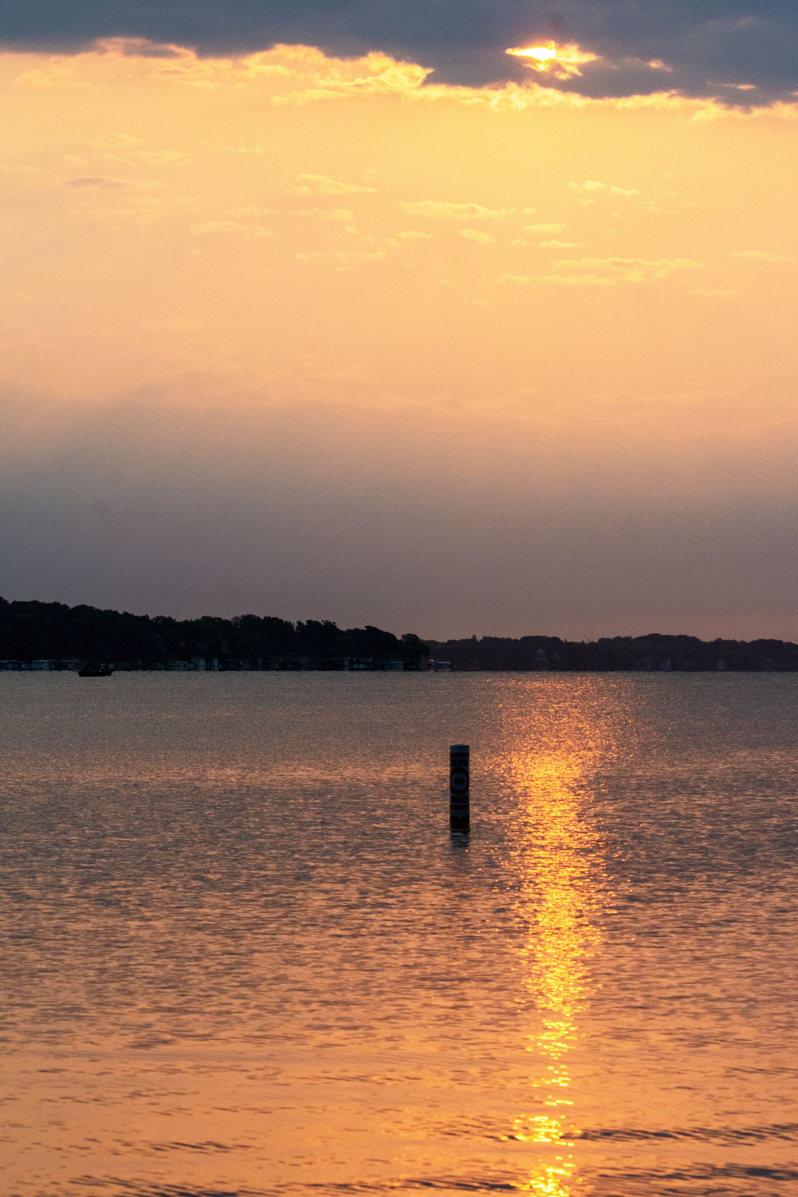 Peaceful summer sunrise reflecting on a calm lake with a single buoy in Waukesha County, Wisconsin. Early morning light in July.
