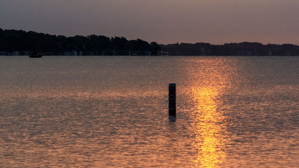 Peaceful summer sunrise reflecting on a calm lake with a single buoy in Waukesha County, Wisconsin. Early morning light in July.