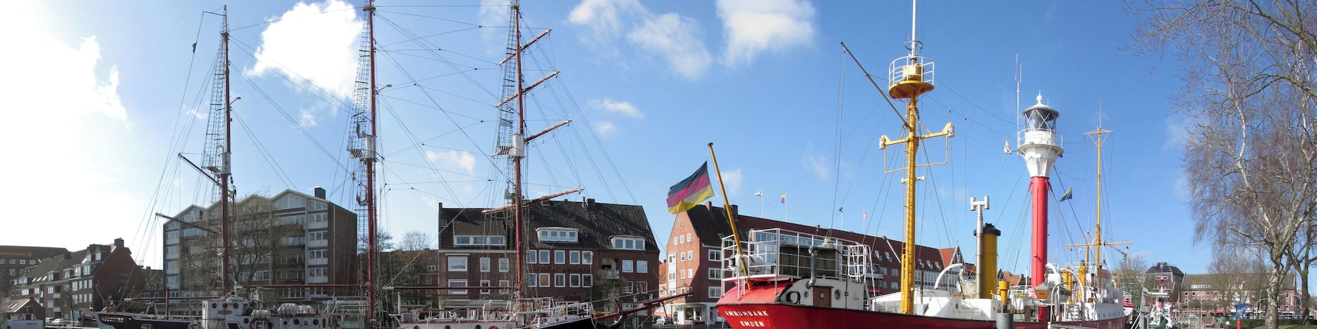Un puerto con barcos altos, una lancha roja llamada 'Willemsburg' y un faro.