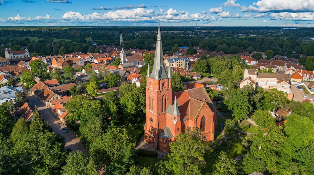 Une ville où se dresse une église remarquable, reconnaissable à son clocher élancé, entourée d’une végétation luxuriante et de bâtiments aux toits rouges.