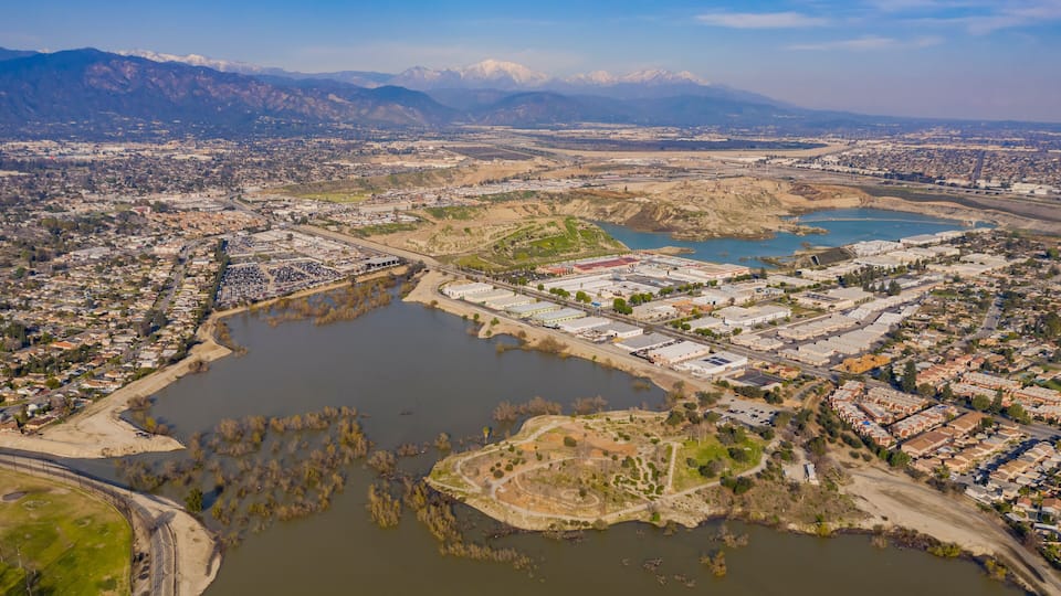 An aerial view of a city with a large lake, industrial buildings, and mountains in the background.