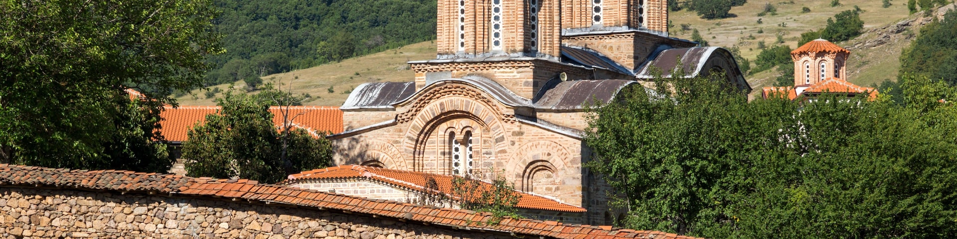 Uma igreja histórica com duas cúpulas, uma parede de pedra e uma paisagem montanhosa ao fundo.