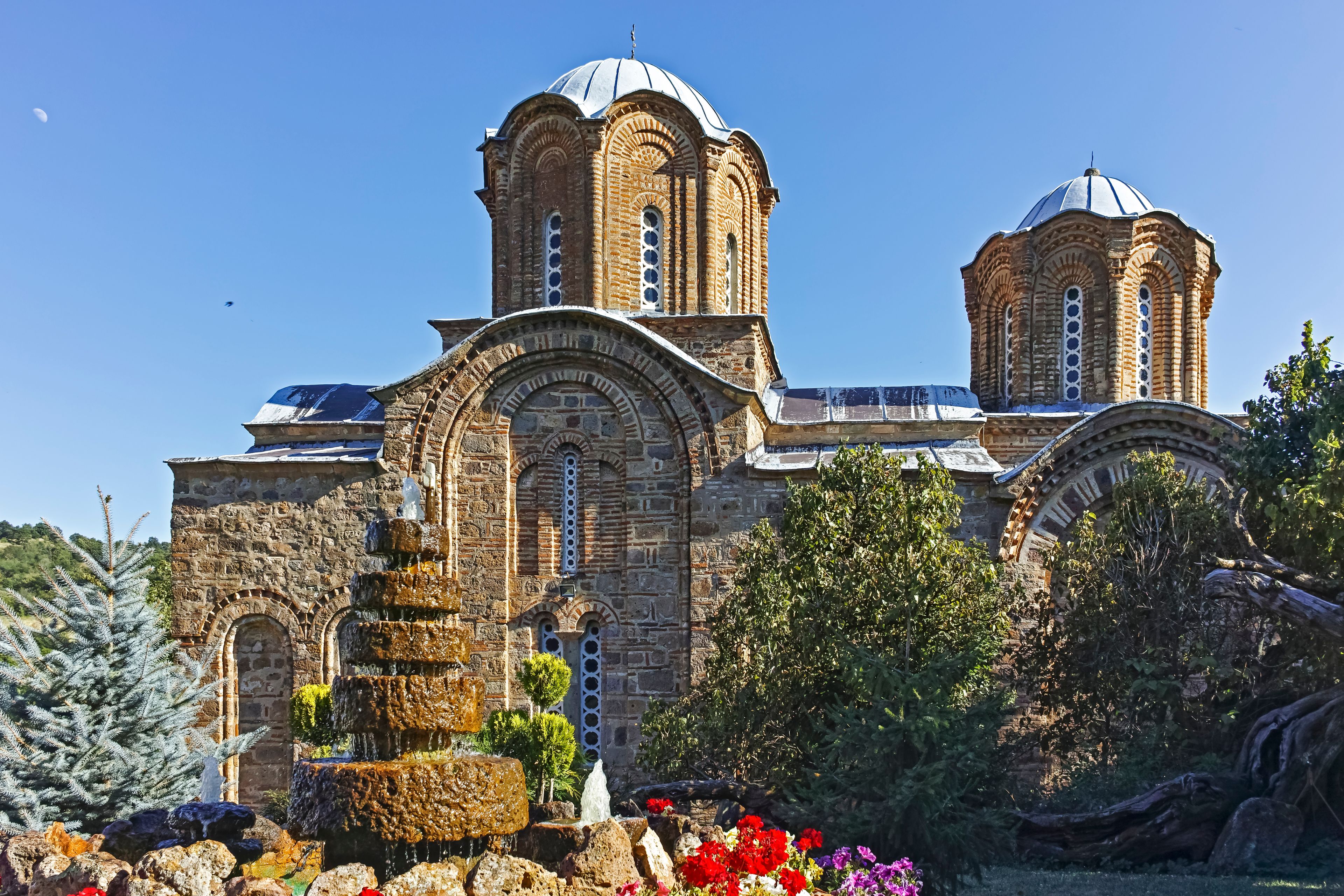 A historic church with two domes, a stone facade, and a fountain in the foreground.