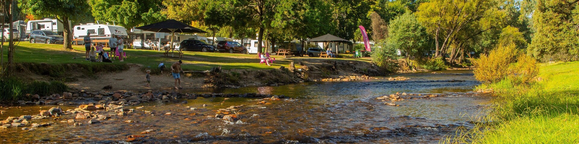 Un río que atraviesa un camping con vehículos recreativos y mesas de picnic.