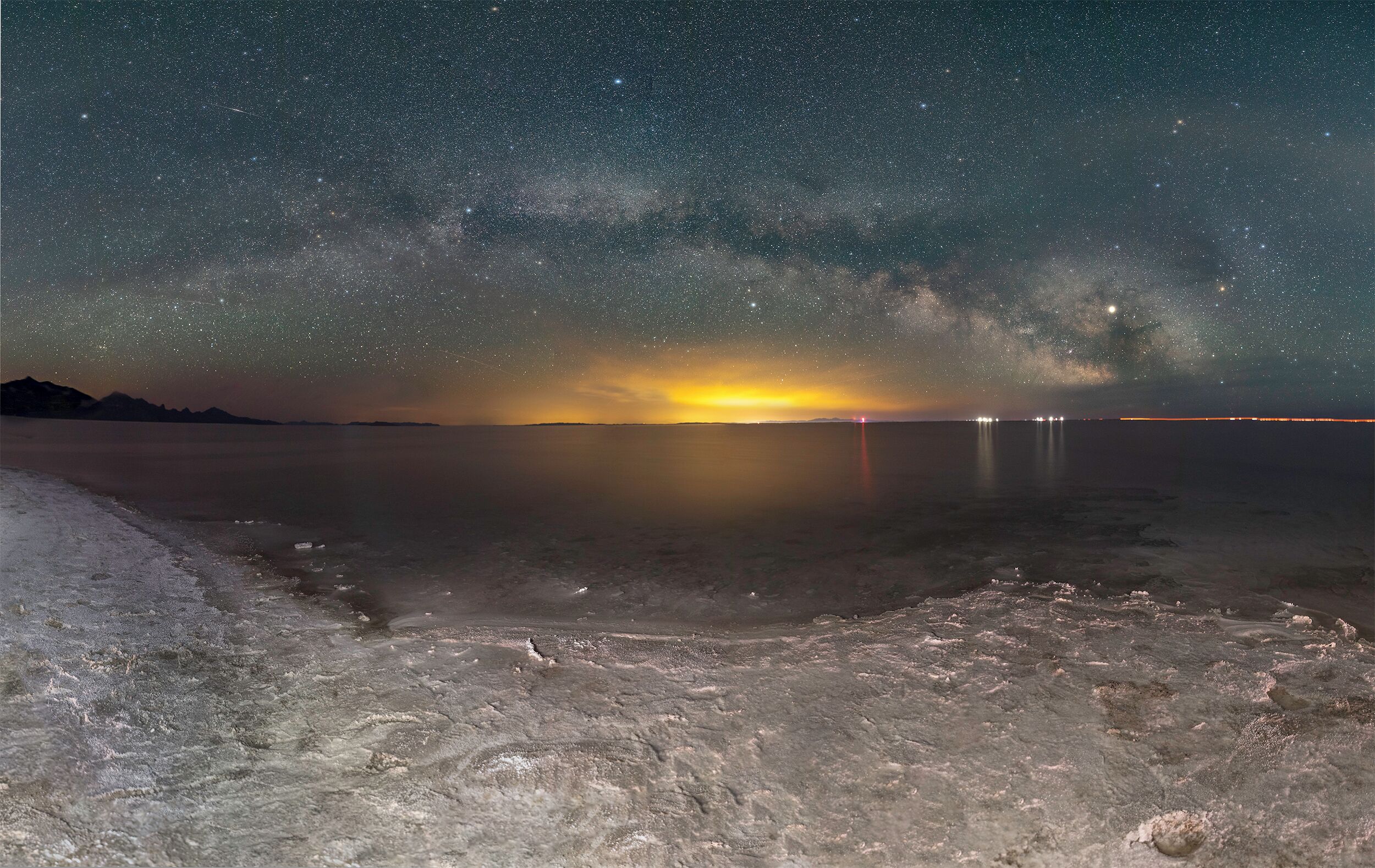 A starry night sky over a calm body of water with a visible Milky Way and distant city lights.