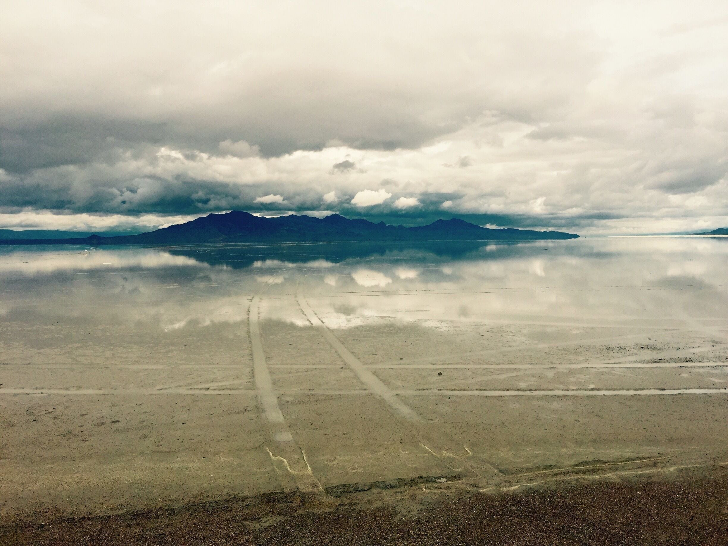 A salt flat with mountain reflections and tire tracks.