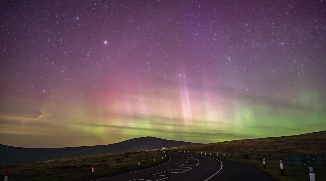 A road curving through a landscape under a starry night sky with the Northern Lights.