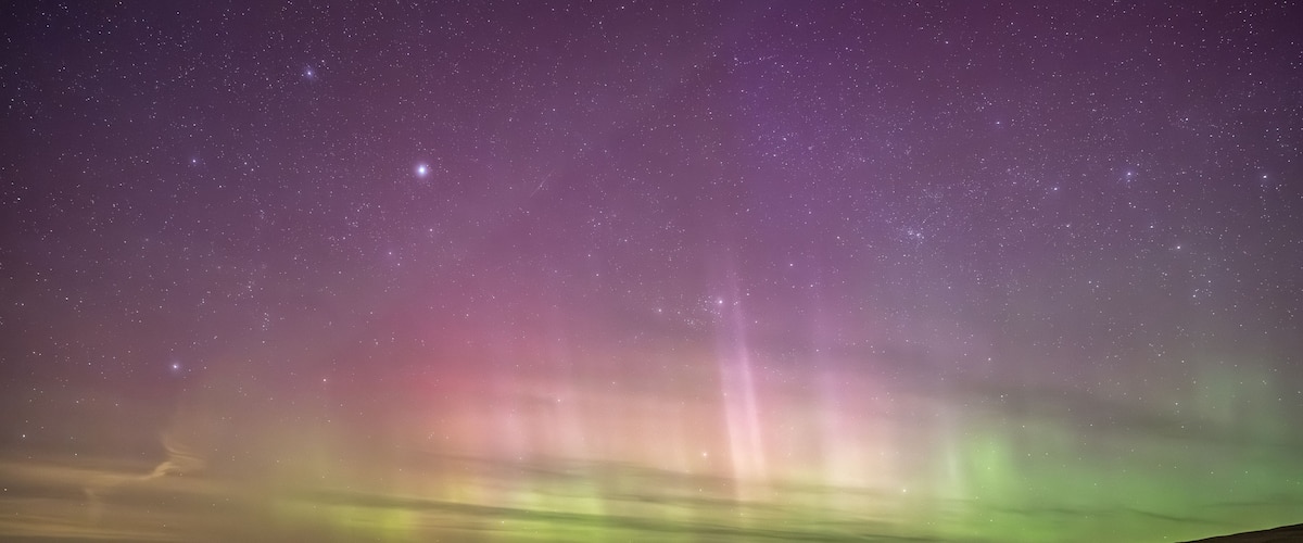 Una carretera serpenteando por un paisaje bajo un cielo estrellado con auroras boreales.