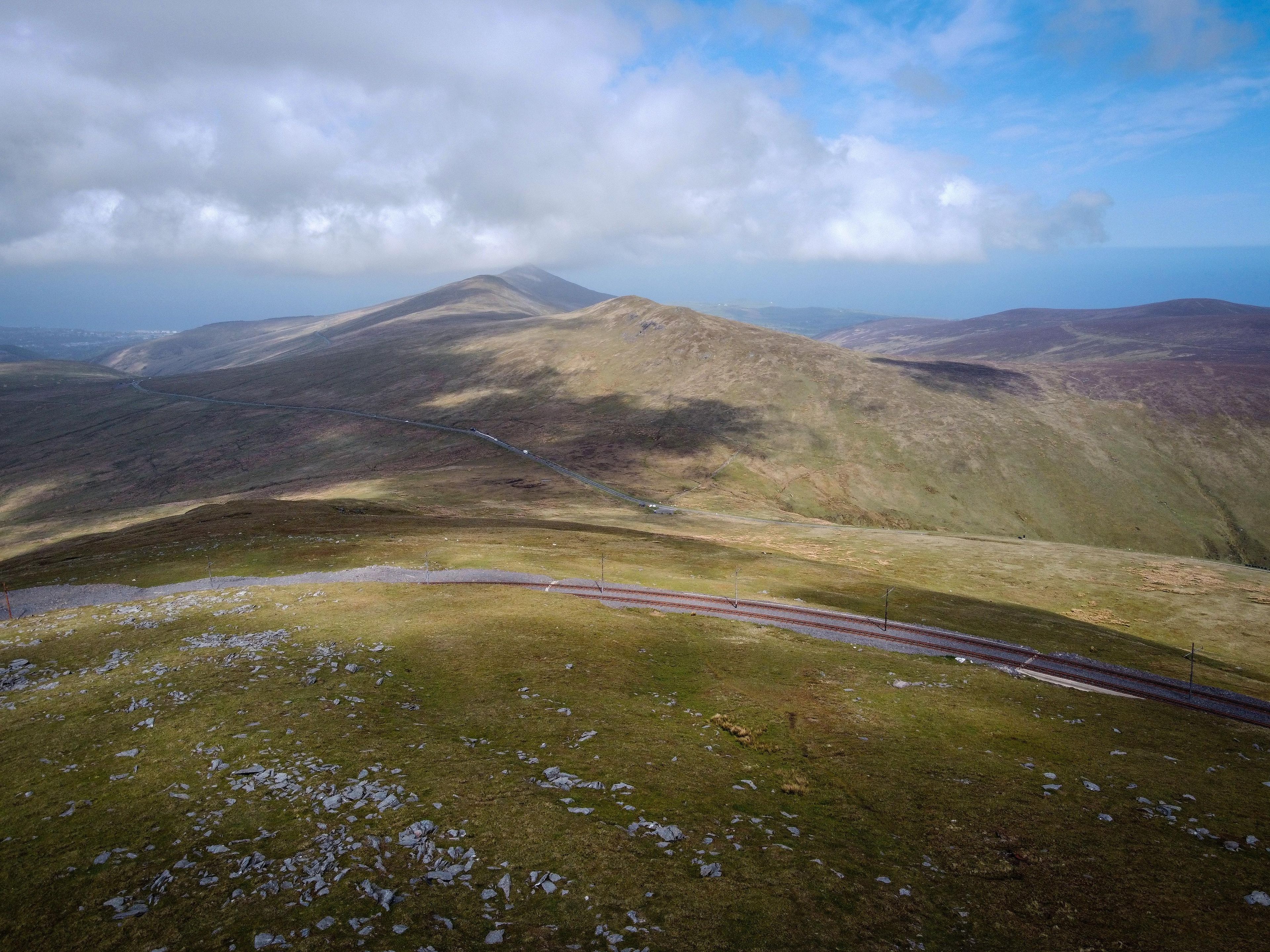 A mountainous landscape with a winding road and a distant mountain peak.