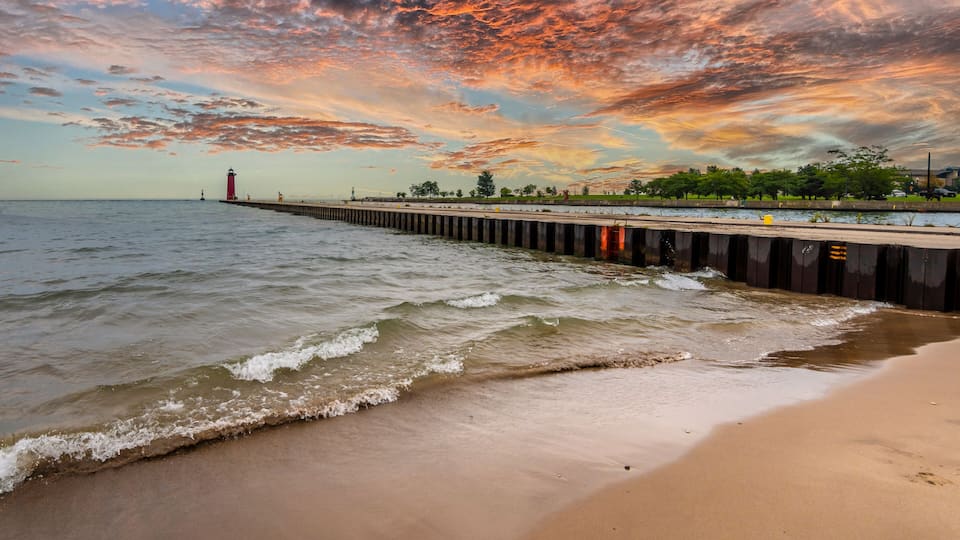 A beach with waves, a pier, and a lighthouse.