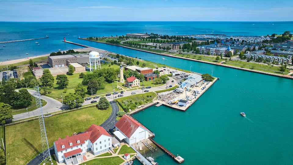 An aerial view of a coastal town with a marina, a lighthouse, and a large water tower.