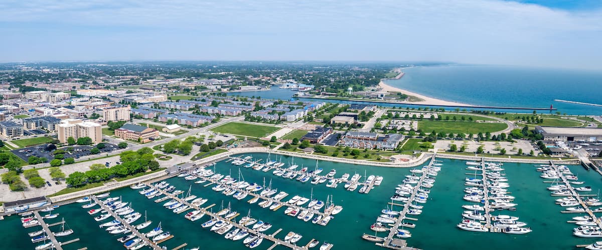 An aerial view of a coastal city with a marina filled with boats, a lighthouse, and a large body of water.