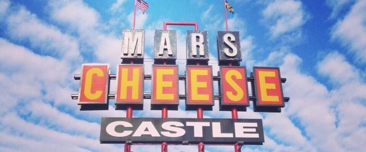 A sign with 'MARS CHEESE CASTLE' written on it, with two flags on top.