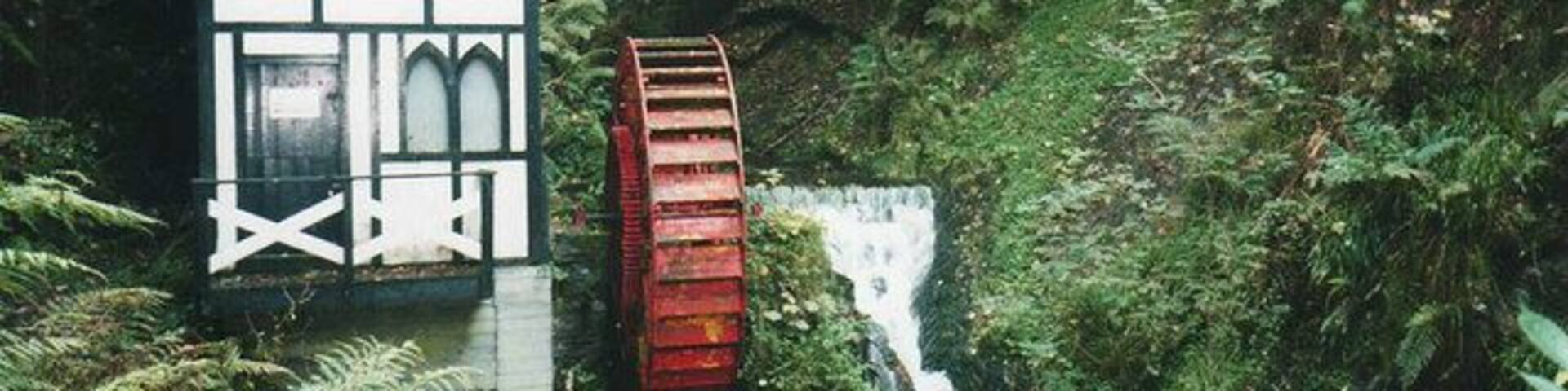 A watermill with a red wheel and a small building with a pointed roof.