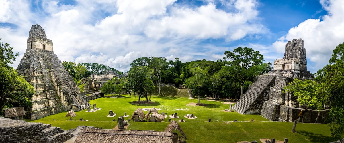 Ancient Mayan ruins with pyramid structures and a well-maintained grassy area.