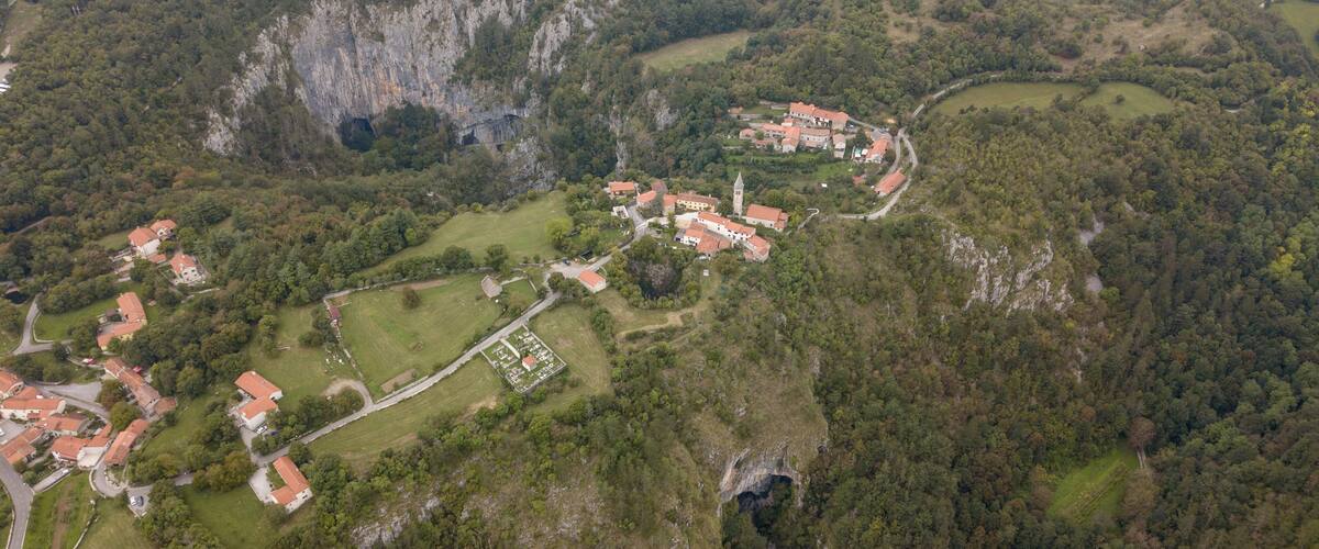 An aerial view of a village with red-roofed houses, a church, and a valley.