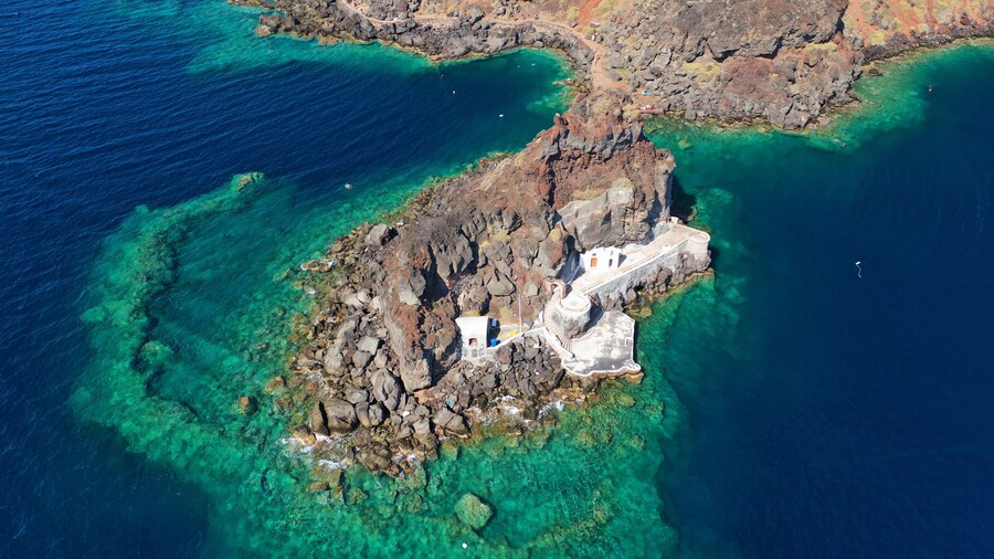 Aerial drone photo of picturesque volcanic with black rock islet and chapel of Agios Nikolaos in bay of Amoudi below iconic village of Oia, Santorini island, Cyclades, Greece