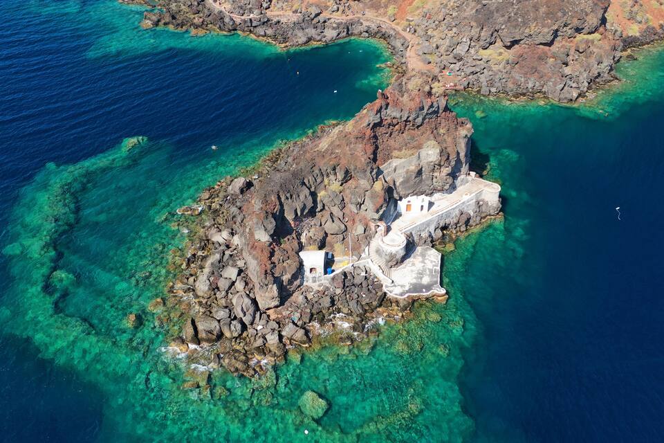 Vista aérea de uma ilha rochosa com águas turquesa cristalinas e um edifício branco.
