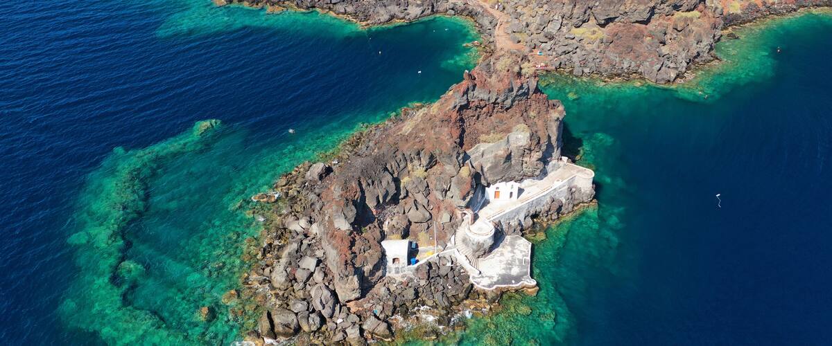 An aerial view of a rocky island with clear turquoise waters and a white building.
