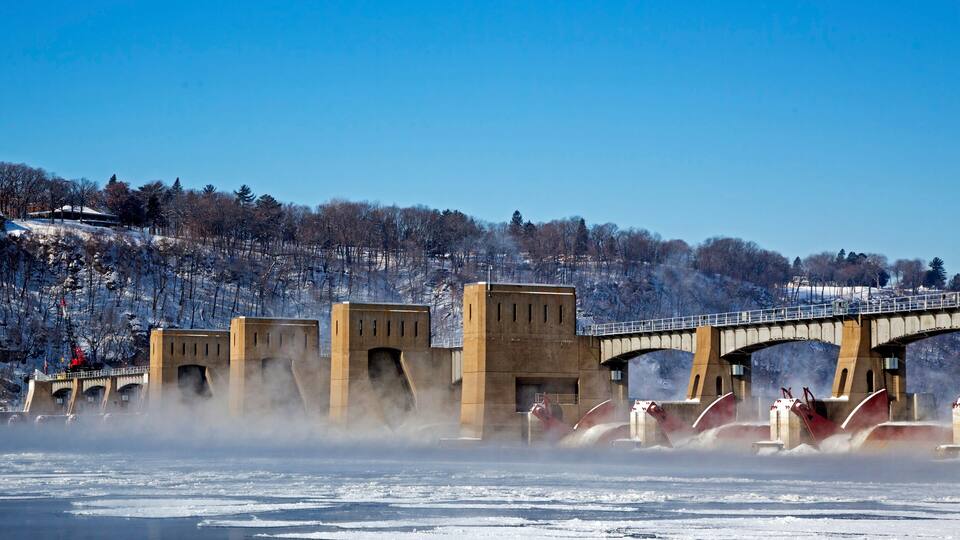 A frozen river with a bridge and snow-covered trees.